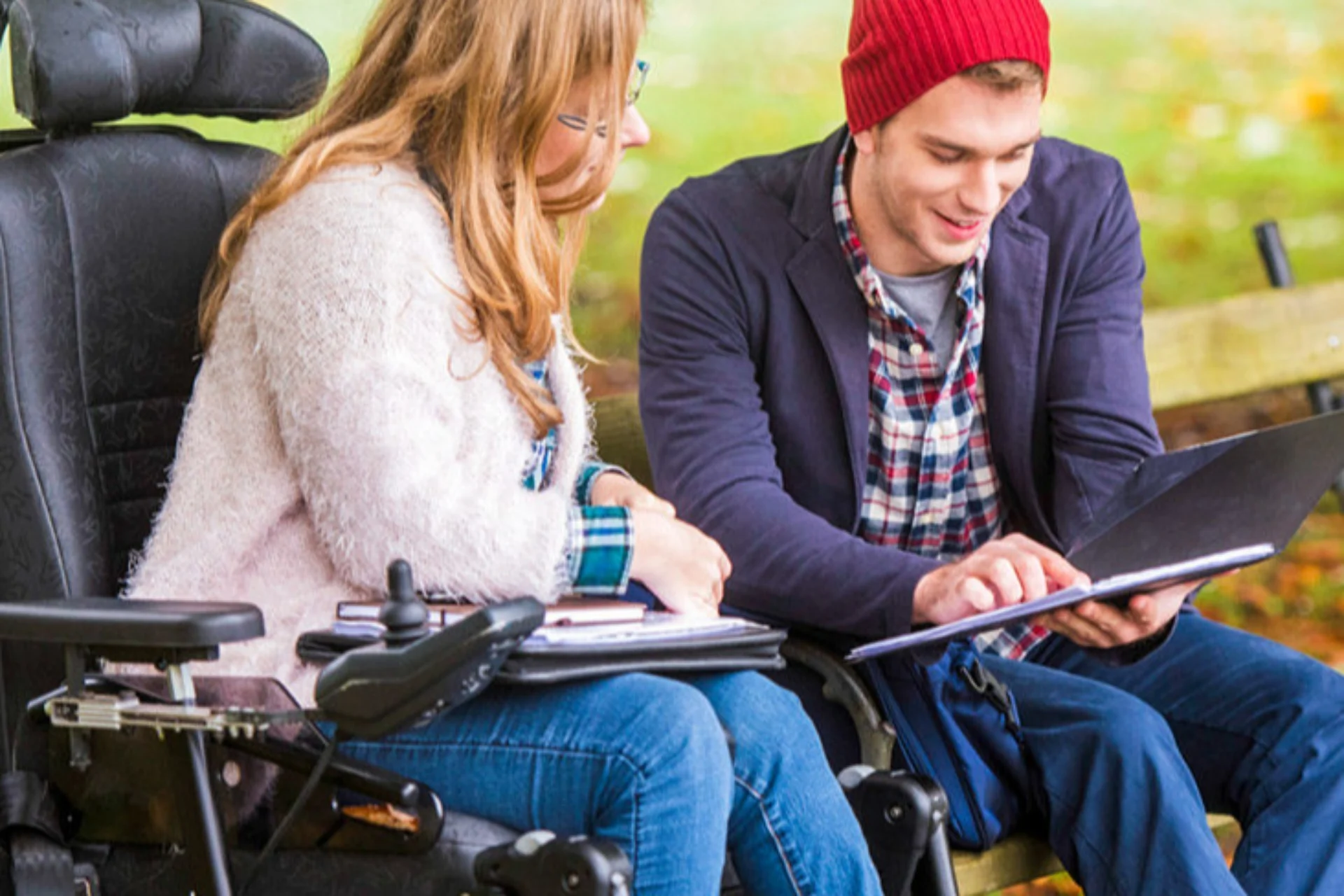two people in wheelchairs looking at a notebook