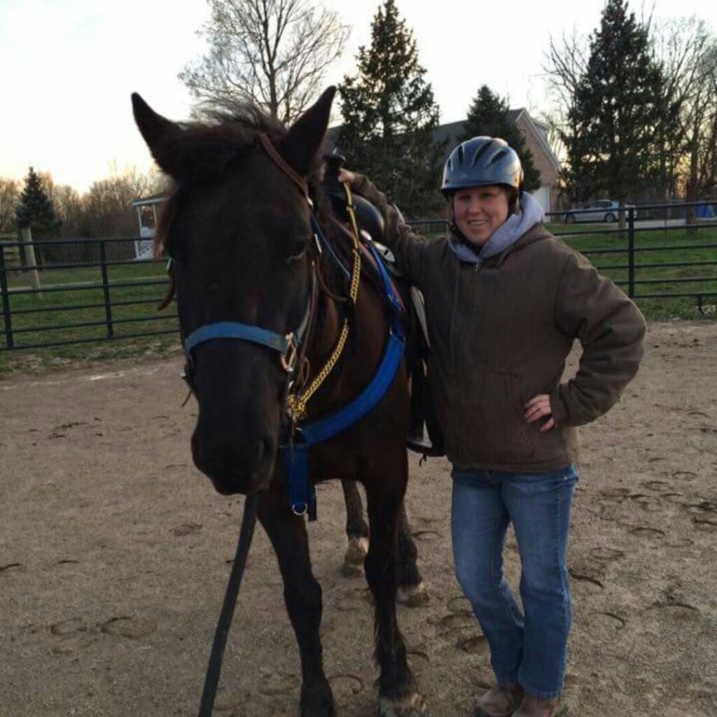 woman in riding helmet standing next to dark brown horse